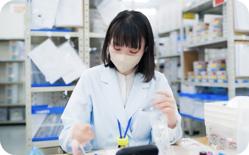 薬剤棚の前で手順書を確認しながら調剤補助をおこなう一般従事者スタッフ